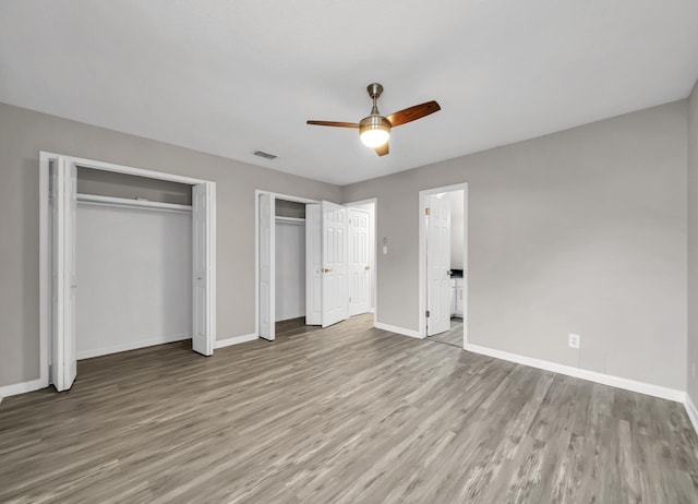 unfurnished bedroom with two closets, light hardwood / wood-style flooring, and ceiling fan