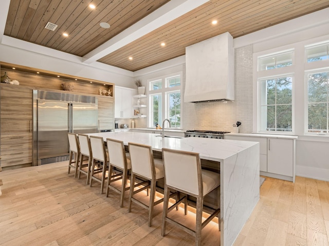 kitchen with premium range hood, white cabinetry, stainless steel built in fridge, a large island, and light hardwood / wood-style floors