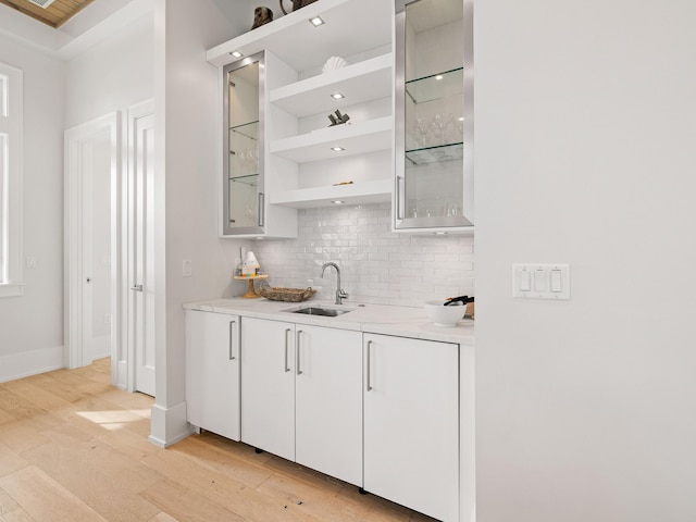 bar with sink, decorative backsplash, light hardwood / wood-style flooring, and white cabinets