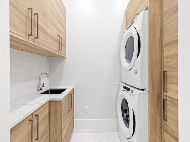 laundry room with cabinets, stacked washing maching and dryer, and sink