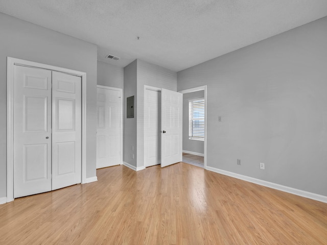 unfurnished bedroom featuring multiple closets, visible vents, light wood-style flooring, electric panel, and baseboards