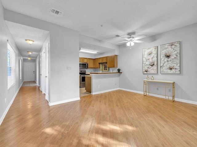 kitchen with visible vents, brown cabinetry, light wood-style flooring, a peninsula, and stainless steel appliances