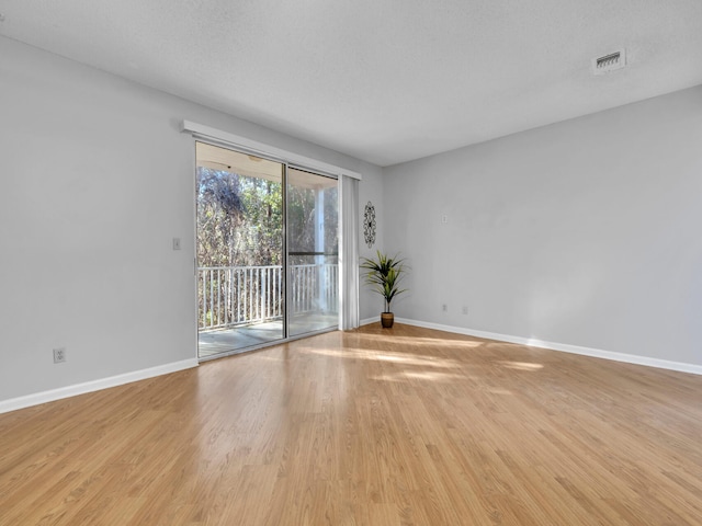 empty room with a textured ceiling, wood finished floors, visible vents, and baseboards