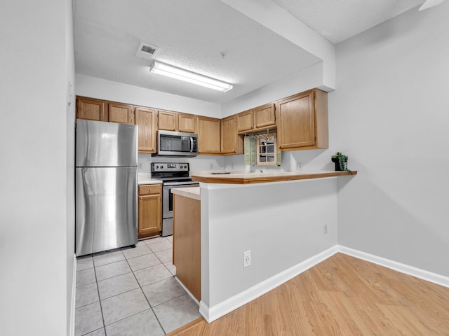 kitchen with visible vents, appliances with stainless steel finishes, a peninsula, light countertops, and a textured ceiling