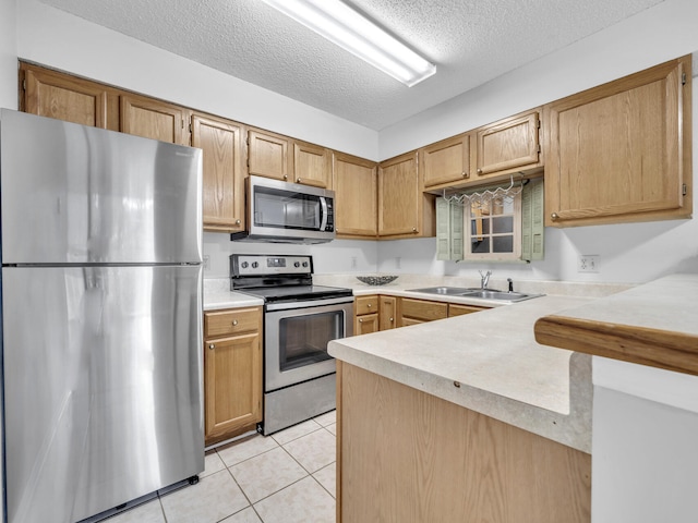 kitchen with appliances with stainless steel finishes, light countertops, a sink, and light tile patterned floors