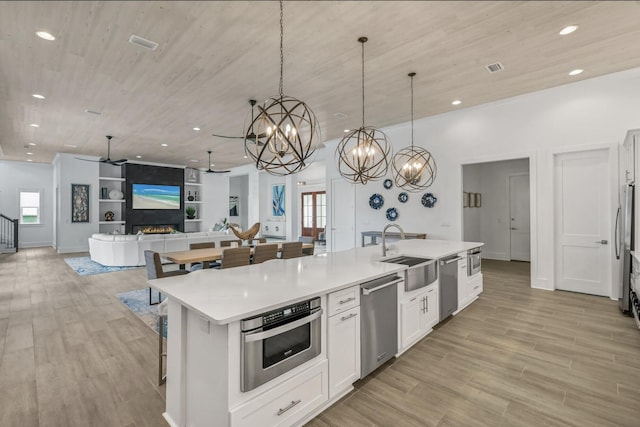 kitchen with white cabinetry, sink, hanging light fixtures, a kitchen island with sink, and stainless steel appliances