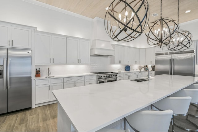 kitchen featuring pendant lighting, sink, high end appliances, an island with sink, and custom range hood