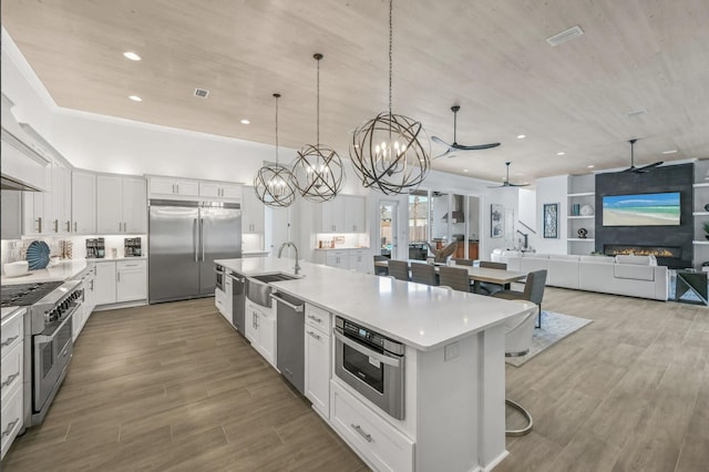 kitchen featuring pendant lighting, a breakfast bar, white cabinetry, high quality appliances, and an island with sink