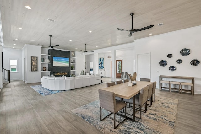 dining area with a fireplace, built in features, ceiling fan, and light wood-type flooring