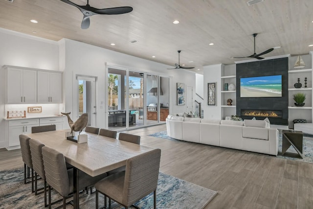 dining room with built in shelves, ceiling fan, a fireplace, and light hardwood / wood-style floors