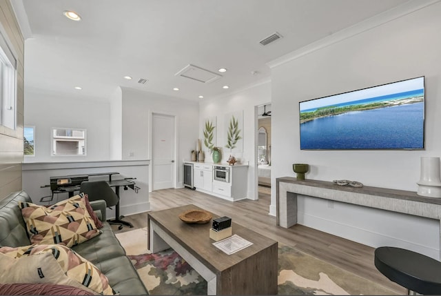 living room with ornamental molding, beverage cooler, and light hardwood / wood-style flooring