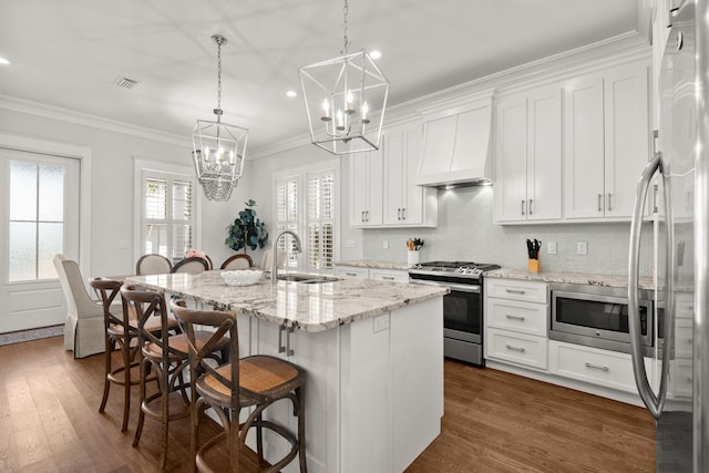 kitchen with stainless steel appliances, a kitchen island with sink, custom exhaust hood, and white cabinets