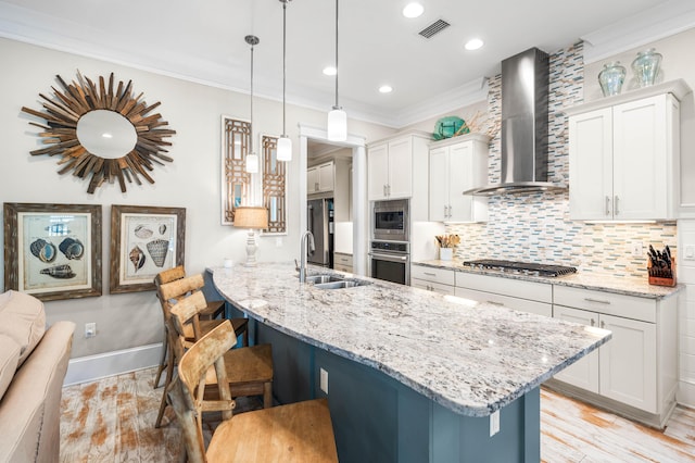 kitchen featuring a breakfast bar, hanging light fixtures, wall chimney range hood, stainless steel appliances, and white cabinets