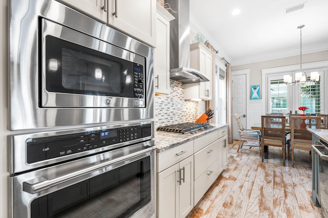 kitchen featuring white cabinetry, stainless steel appliances, crown molding, light stone countertops, and wall chimney exhaust hood