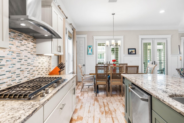 kitchen with wall chimney exhaust hood, crown molding, green cabinetry, appliances with stainless steel finishes, and white cabinets