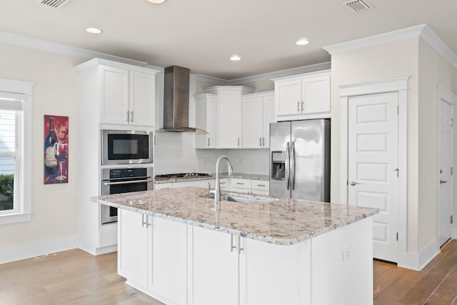 kitchen with light wood-style flooring, a sink, visible vents, appliances with stainless steel finishes, and wall chimney exhaust hood