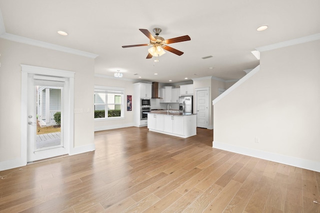 unfurnished living room featuring crown molding, a sink, ceiling fan, and light wood finished floors