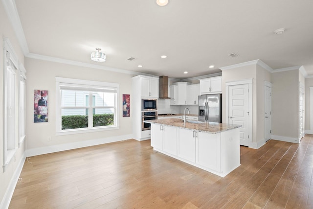 kitchen featuring white cabinets, ornamental molding, appliances with stainless steel finishes, light wood-type flooring, and wall chimney range hood