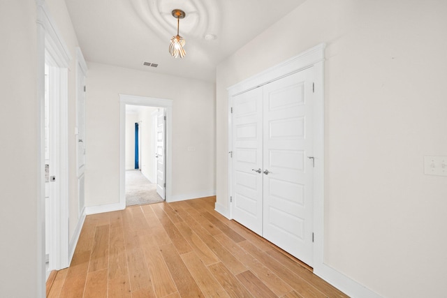 hall featuring light wood-type flooring, visible vents, and baseboards