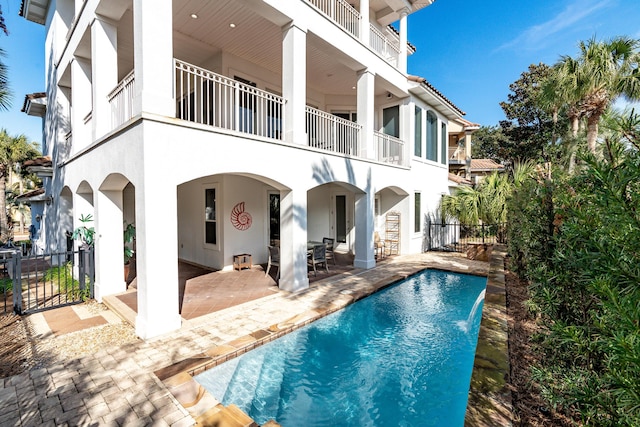 back of property featuring pool water feature, a balcony, a fenced in pool, and a patio