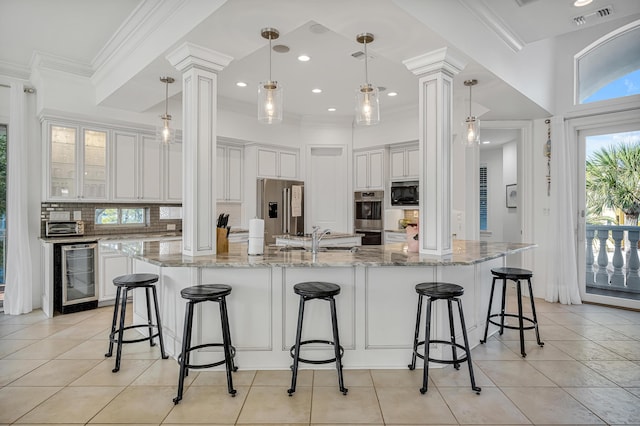 kitchen featuring sink, stainless steel appliances, wine cooler, light stone countertops, and decorative light fixtures