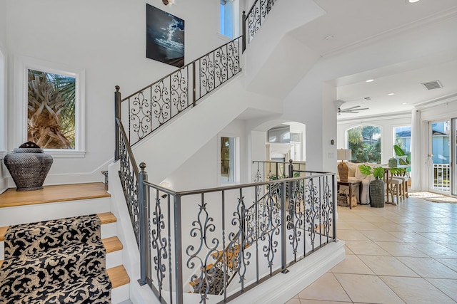 stairway featuring tile patterned flooring, a towering ceiling, ornamental molding, and ceiling fan