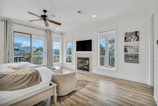 bedroom with a tiled fireplace, access to outside, ceiling fan, crown molding, and light hardwood / wood-style flooring