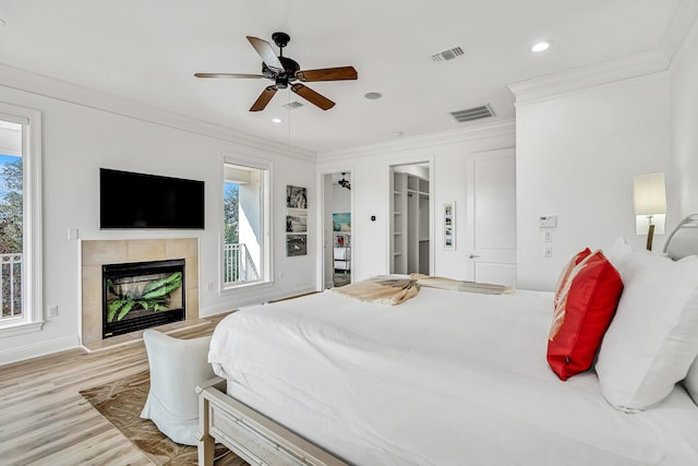 bedroom featuring crown molding, ceiling fan, a fireplace, and light hardwood / wood-style flooring