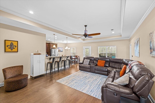 living room with ceiling fan, wood finished floors, baseboards, ornamental molding, and a tray ceiling