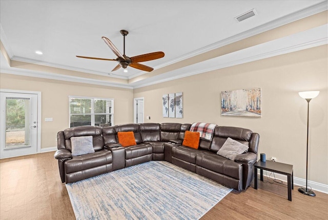 living room featuring baseboards, visible vents, ornamental molding, wood finished floors, and a tray ceiling