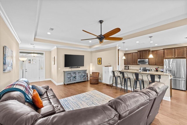 living room featuring a raised ceiling, ornamental molding, ceiling fan, and light hardwood / wood-style flooring