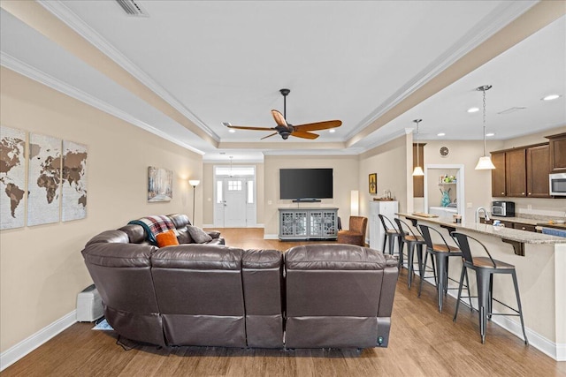 living area with crown molding, a tray ceiling, and wood finished floors