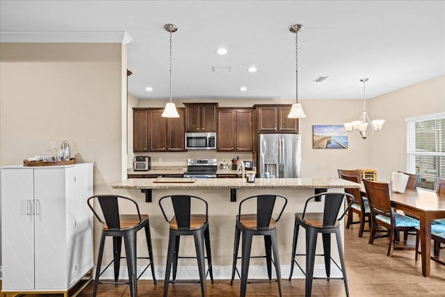 kitchen with a breakfast bar area, appliances with stainless steel finishes, light stone counters, dark brown cabinets, and a chandelier