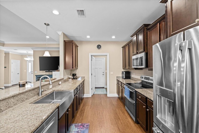 kitchen featuring sink, decorative light fixtures, stainless steel appliances, light stone countertops, and light hardwood / wood-style floors