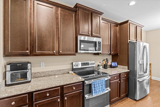 kitchen featuring appliances with stainless steel finishes, light wood-type flooring, dark brown cabinetry, and light stone countertops