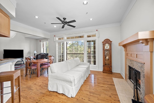 living room with a tiled fireplace, crown molding, ceiling fan, and light wood-type flooring