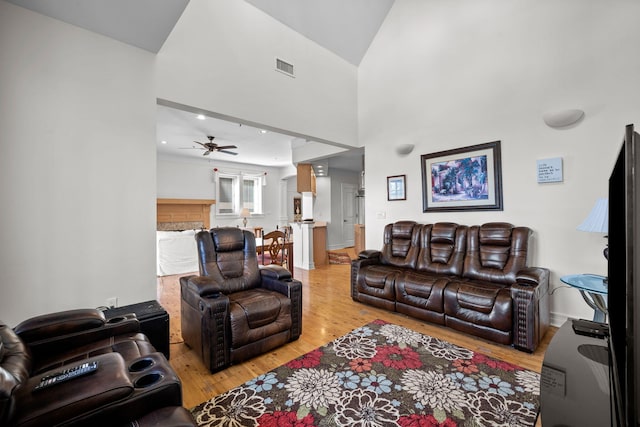 living room featuring light hardwood / wood-style floors, ceiling fan, and a high ceiling