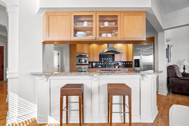 kitchen featuring stainless steel appliances, a kitchen breakfast bar, light stone counters, and range hood