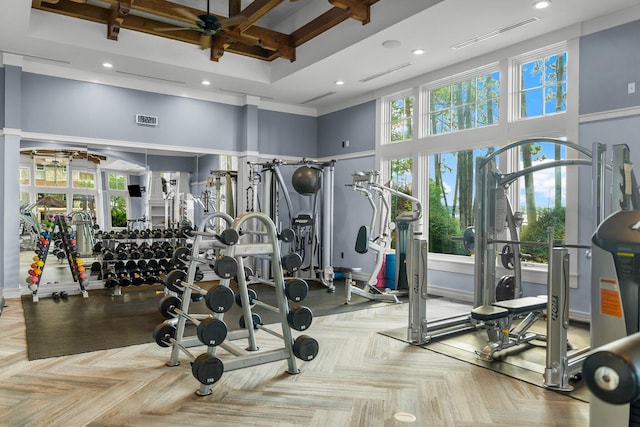 gym with ceiling fan, light parquet flooring, and a high ceiling