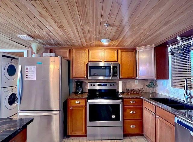 kitchen with appliances with stainless steel finishes, sink, dark stone countertops, stacked washer and clothes dryer, and wood ceiling