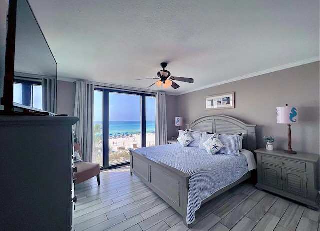 bedroom featuring a beach view, a water view, crown molding, a textured ceiling, and ceiling fan