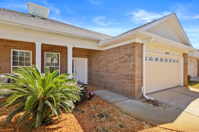 view of exterior entry featuring brick siding, concrete driveway, a garage, and a shingled roof