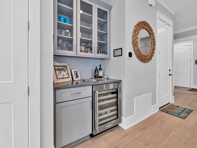 bar featuring gray cabinetry, crown molding, light hardwood / wood-style flooring, and beverage cooler