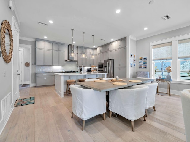 dining area featuring ornamental molding, sink, and light hardwood / wood-style flooring