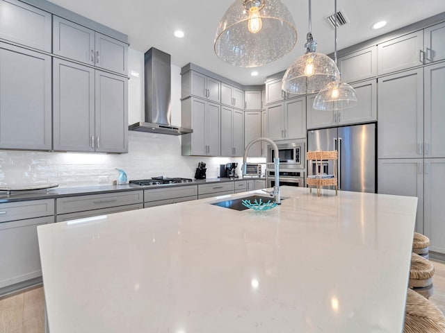 kitchen featuring appliances with stainless steel finishes, gray cabinets, light stone countertops, and wall chimney range hood