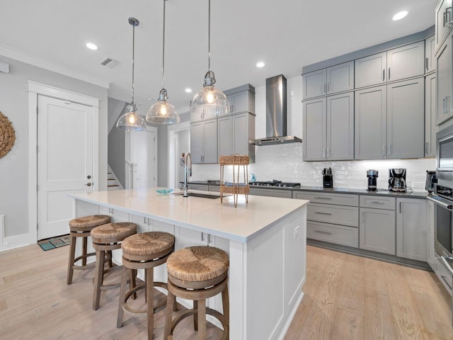 kitchen featuring pendant lighting, a kitchen breakfast bar, an island with sink, and wall chimney range hood