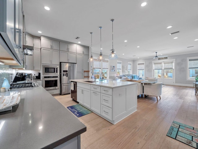 kitchen with sink, hanging light fixtures, a center island with sink, light hardwood / wood-style flooring, and appliances with stainless steel finishes