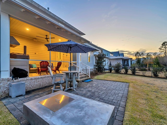 patio terrace at dusk featuring ceiling fan, an outdoor fire pit, and a lawn