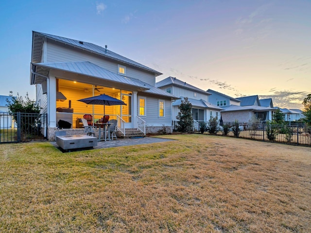 back house at dusk with a patio area and a lawn