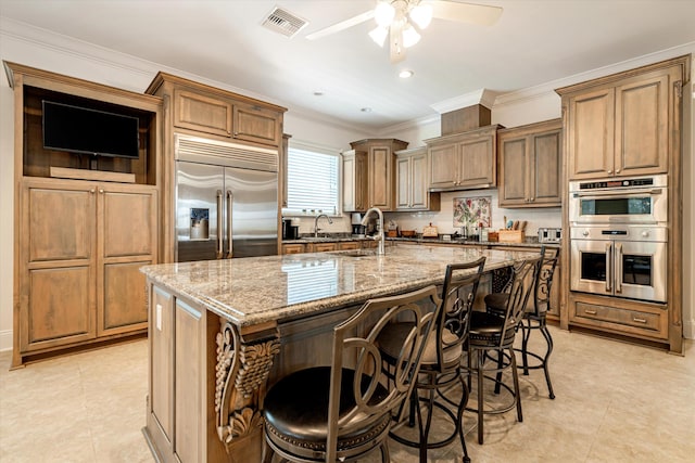 kitchen with sink, a breakfast bar area, a kitchen island with sink, stainless steel appliances, and light stone countertops